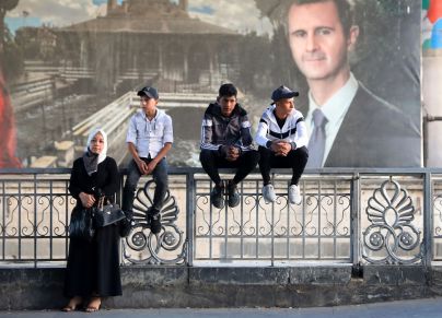 عائلات سورية تنتظر أمام صورة الأسد