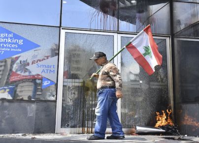 (Getty) لبناني يحمل علم بلاده أمام بنك تعرض للتخريب