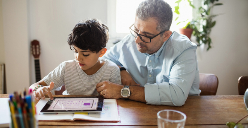 Father assisting son in using digital tablet at home