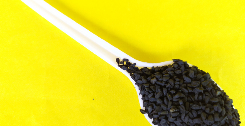 Black Cumin Seeds On Spoon, Yellow Background.