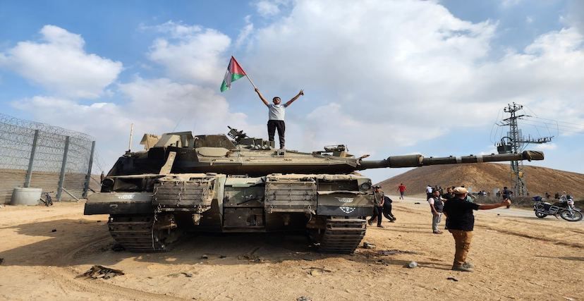 فلسطينيون يحتفلون من أمام دبابة إسرائيلية محترقة في غلاف غزة
