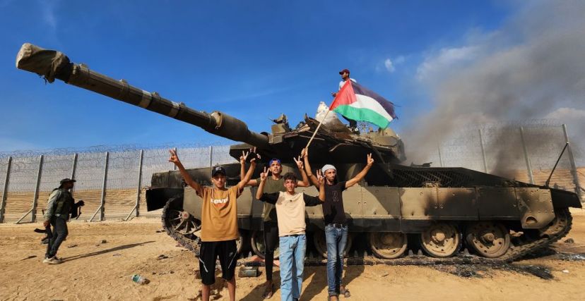 فلسطينيون يحتفلون قرب دبابة إسرائيلية محترقة في غلاف غزة (Getty)