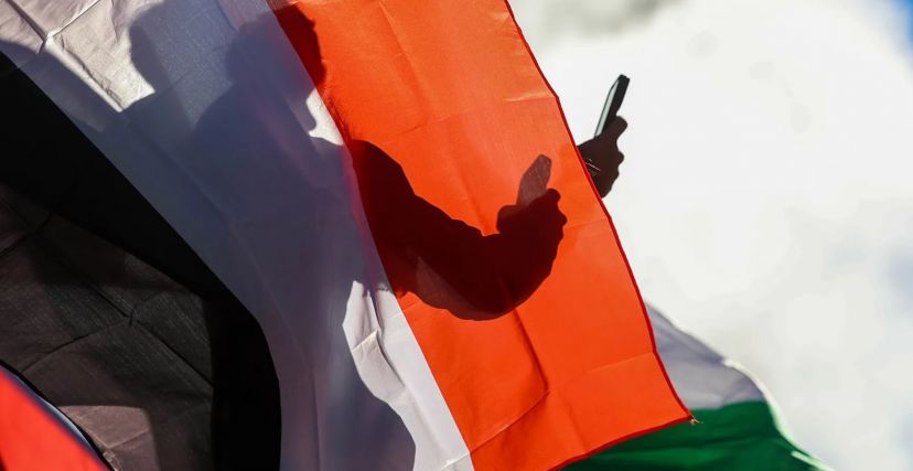 رجل خلف علم فلسطين يحمل هاتفًا