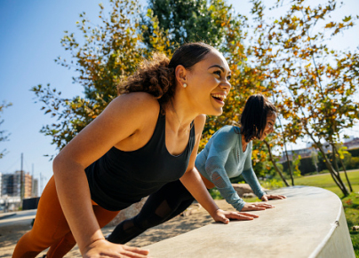 Cheerful women doing push-ups on retaining wall at park