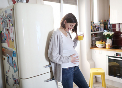 Pregnant woman drinking orange juice in kitchen