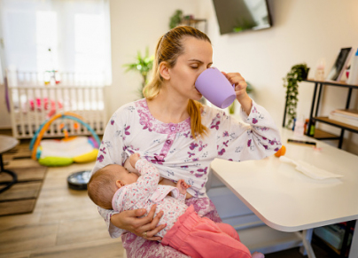 Mother drinking coffee while breastfeeding her newborn baby