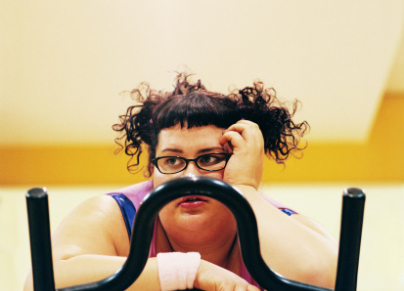 Contemplative Overweight Woman on an Exercise Bike in the Gym